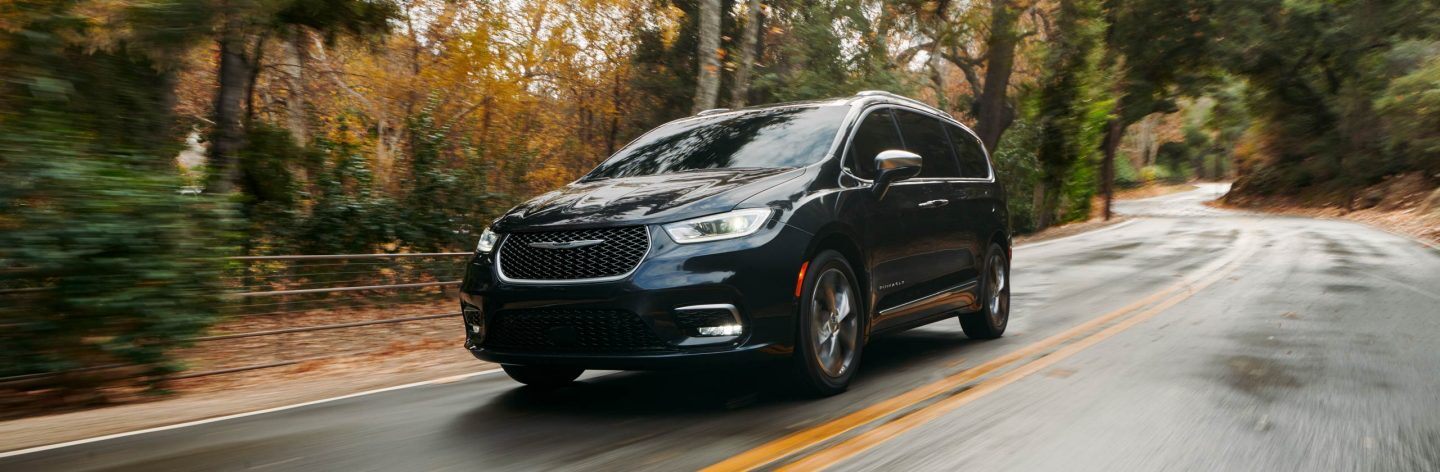 The 2022 Chrysler Pacifica Pinnacle being driven on a road lined with autumn foliage.