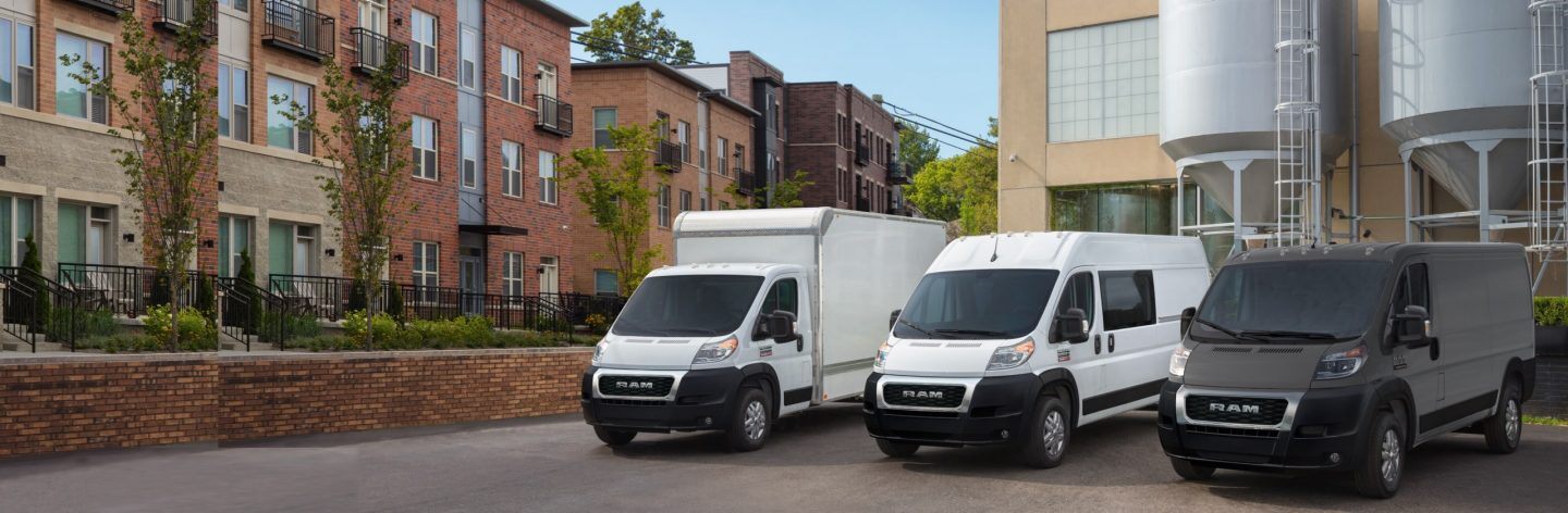 A lineup of a 2022 Ram ProMaster Cutaway Van with box upfit, a 2022 Ram ProMaster Cargo Crew Van and a 2022 Ram ProMaster Cargo Van parked beside an industrial building.