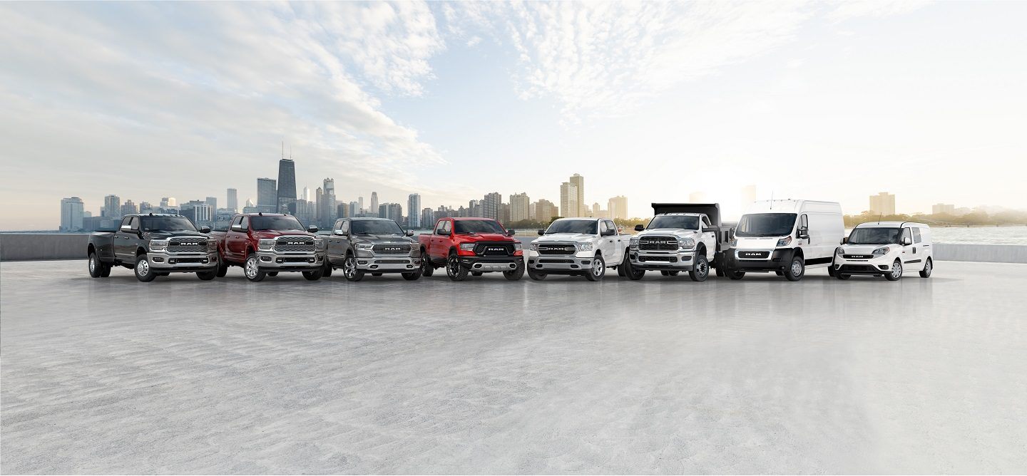 A lineup of eight 2021 Ram trucks and vans with a city skyline in the distance.
