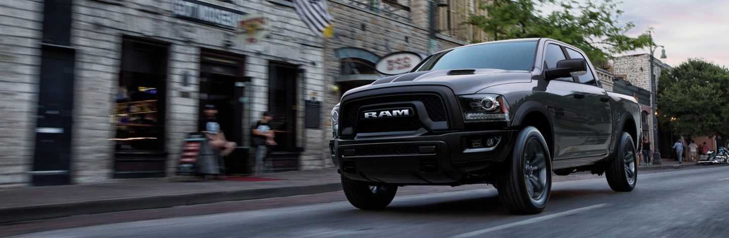 A 2023 Ram 1500 Classic Warlock Crew Cab being driven down a city street with the background blurred to indicate the vehicle is in motion.