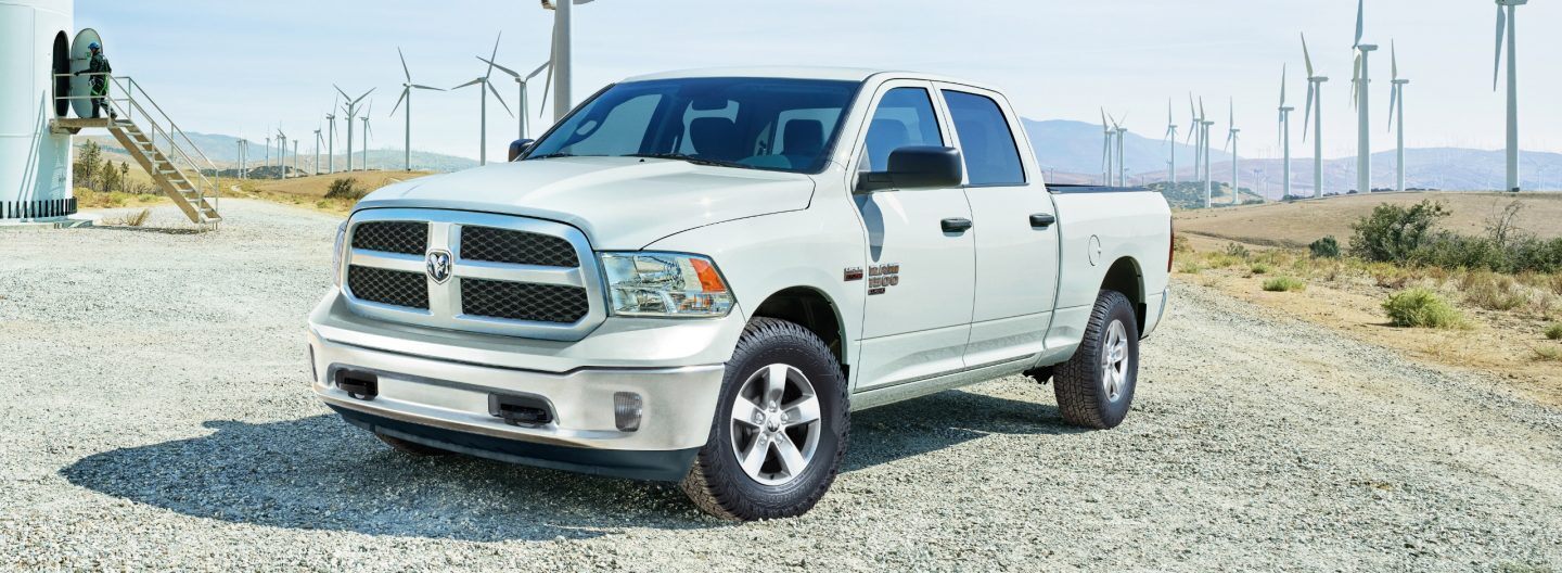 A driver-side front angle of a white 2024 Ram 1500 Classic Tradesman 4x4 Crew Cab parked at a windmill farm.